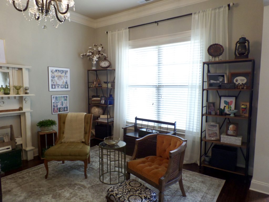 Mismatched antique chairs in front of a large window with sheer curtains.