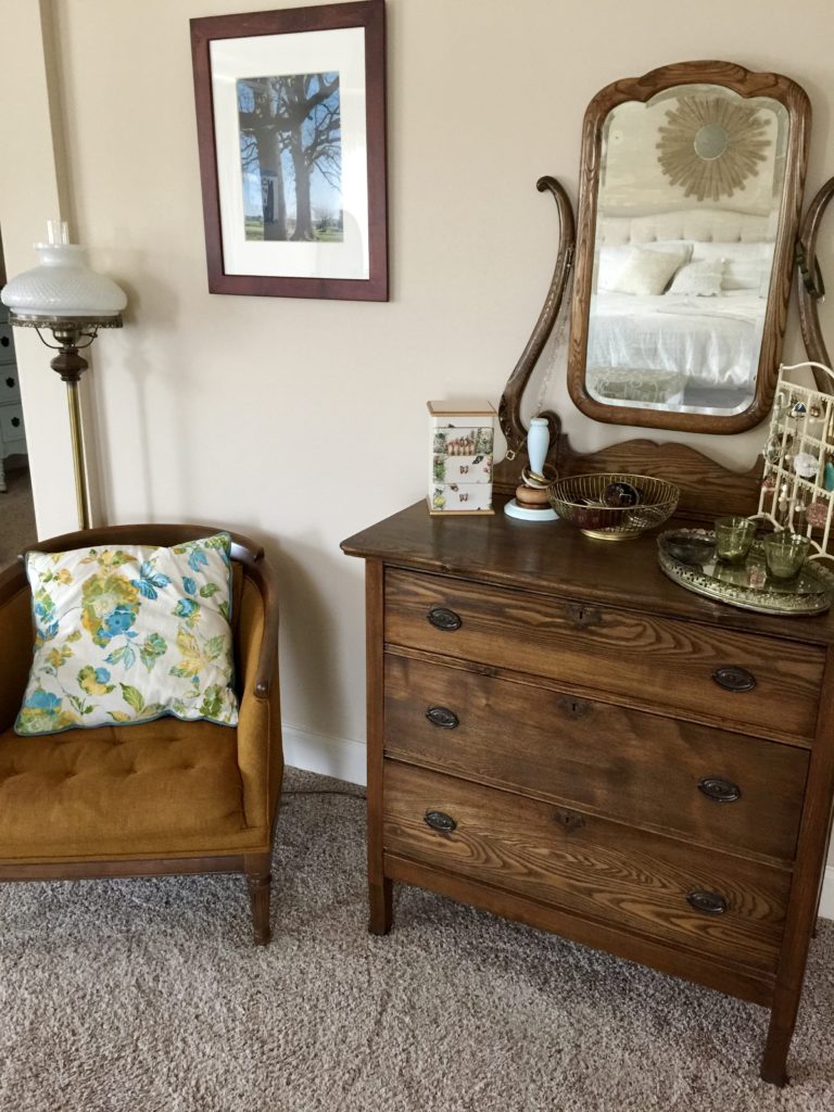 A vintage dresser with a mirror and antique decor next to a vintage chair.