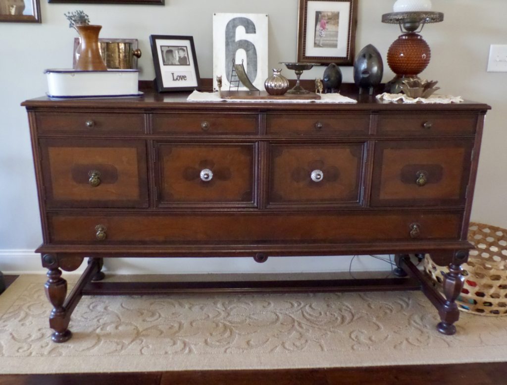 A large antique sideboard in the entryway of a home with vintage decor on top.