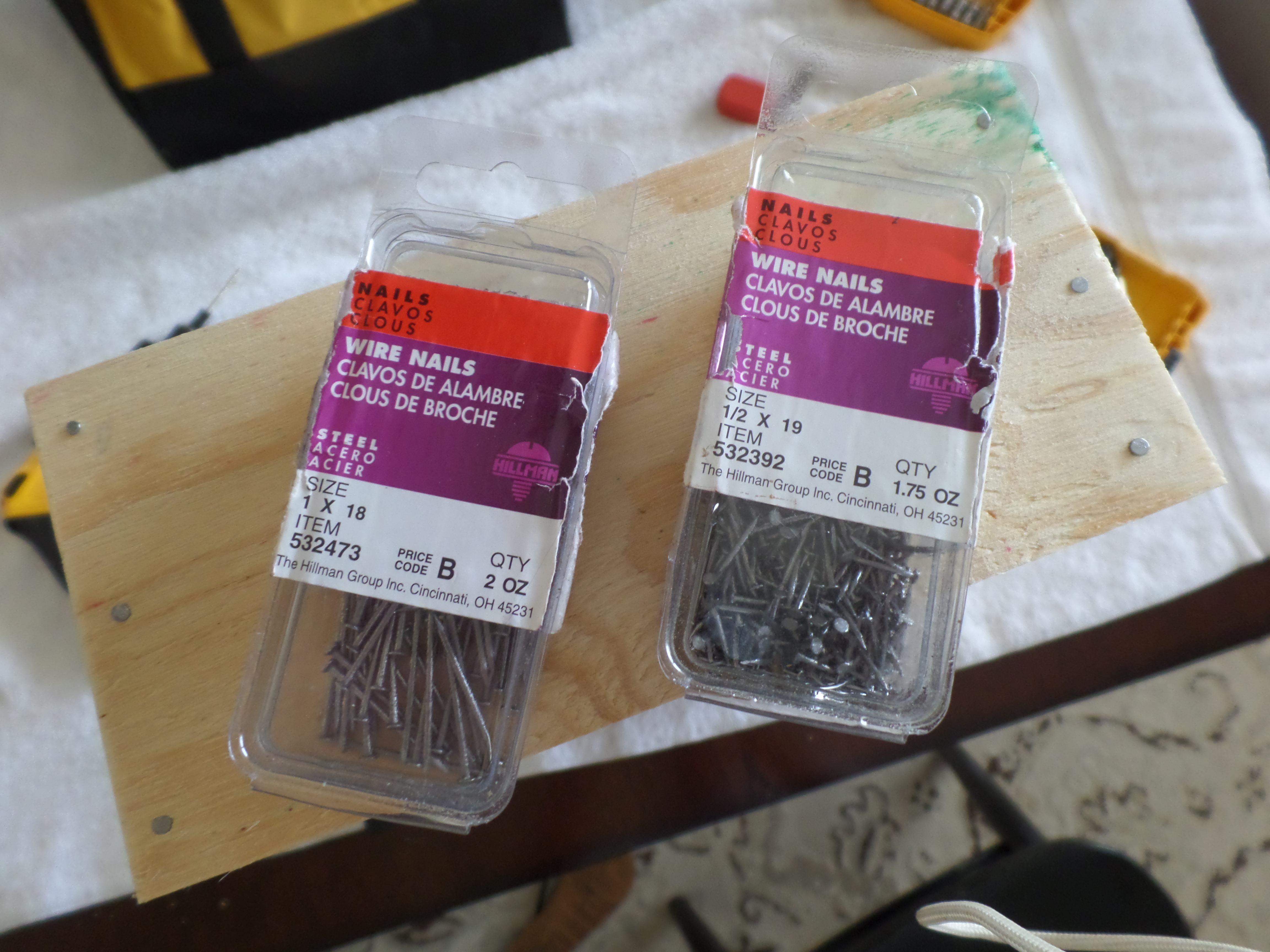 Two boxes of screws on a piece of wood on a dining room table.