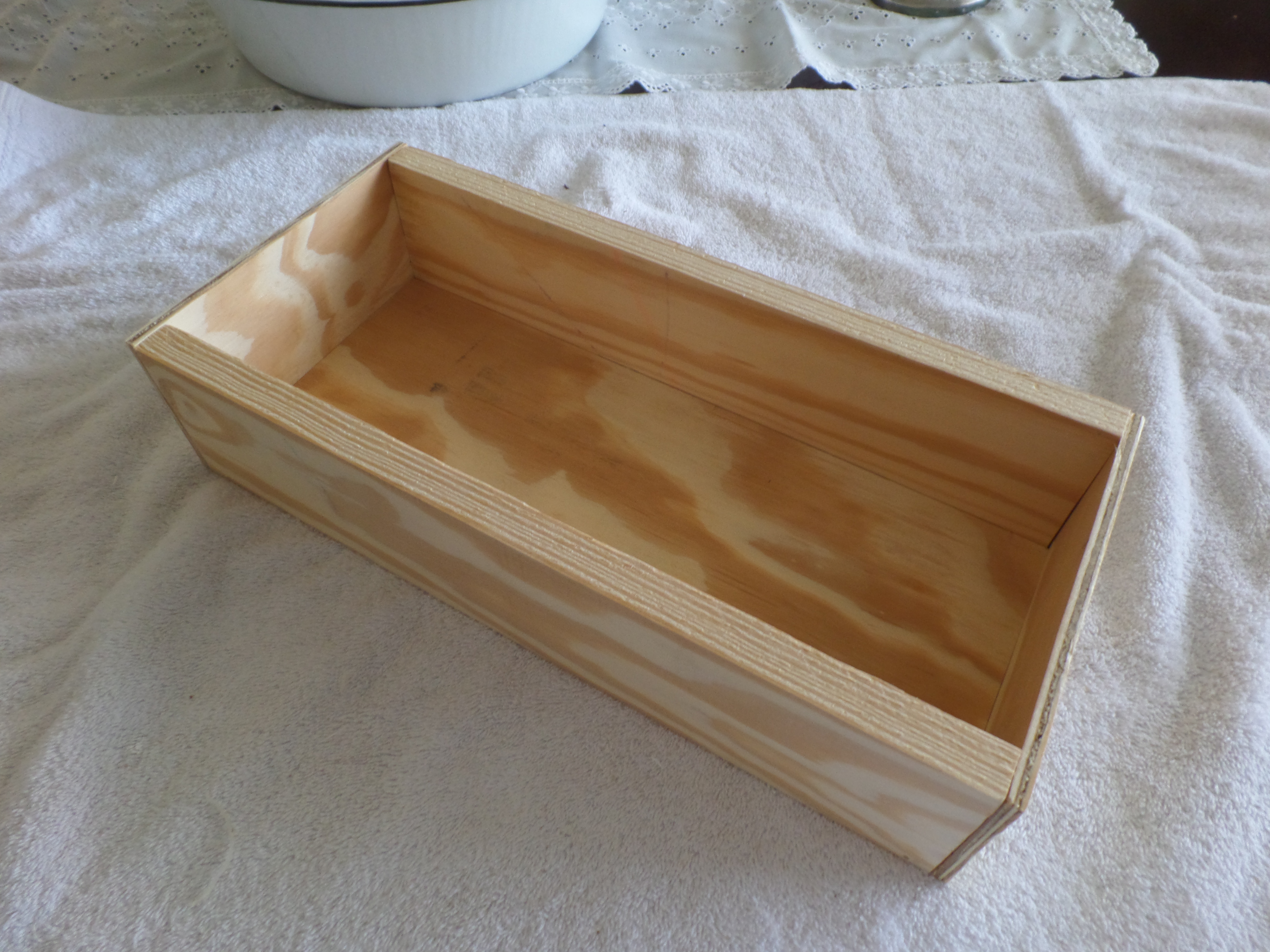 An unfinished rectangular wooden box on a white towel.