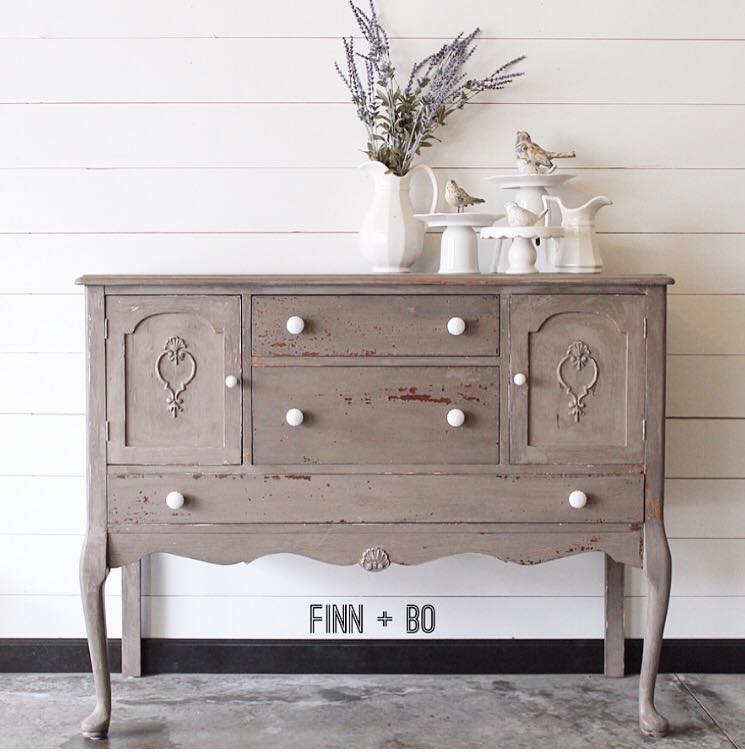 A farmhouse side table with gray-brown milk paint finish and decor on top.