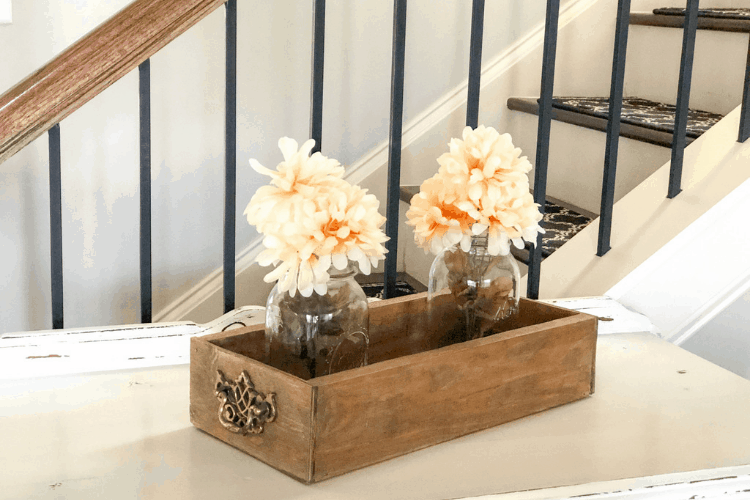 Two mason glass jar flower arrangements inside a wooden crate on a table.