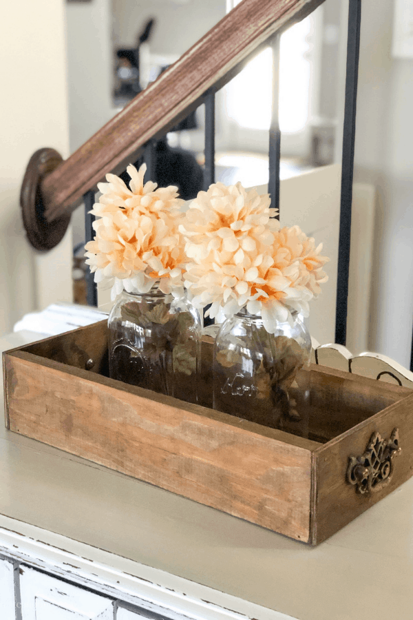 A farmhouse-style crate with two peach floral arrangements inside two mason glass jars.