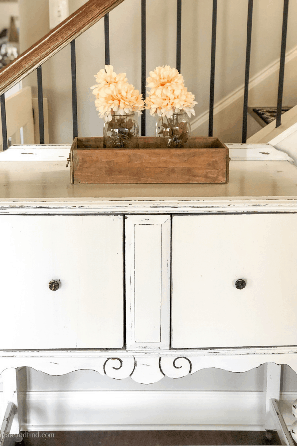 A DIY wooden crate sits on an antique sideboard with two mason glass jars with orange flowers inside.