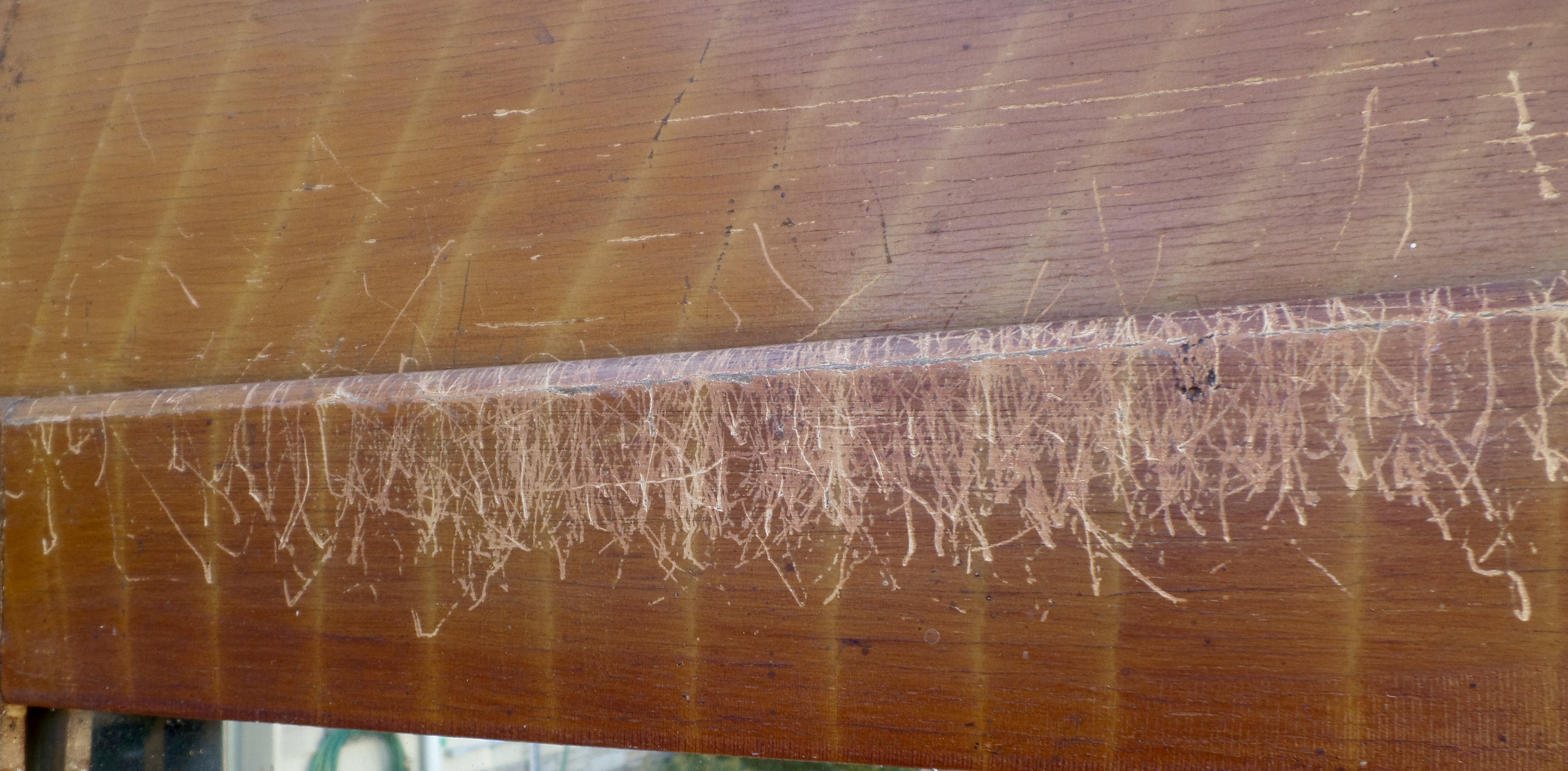 Lots of scratch marks on the top of an antique wood piece of furniture.