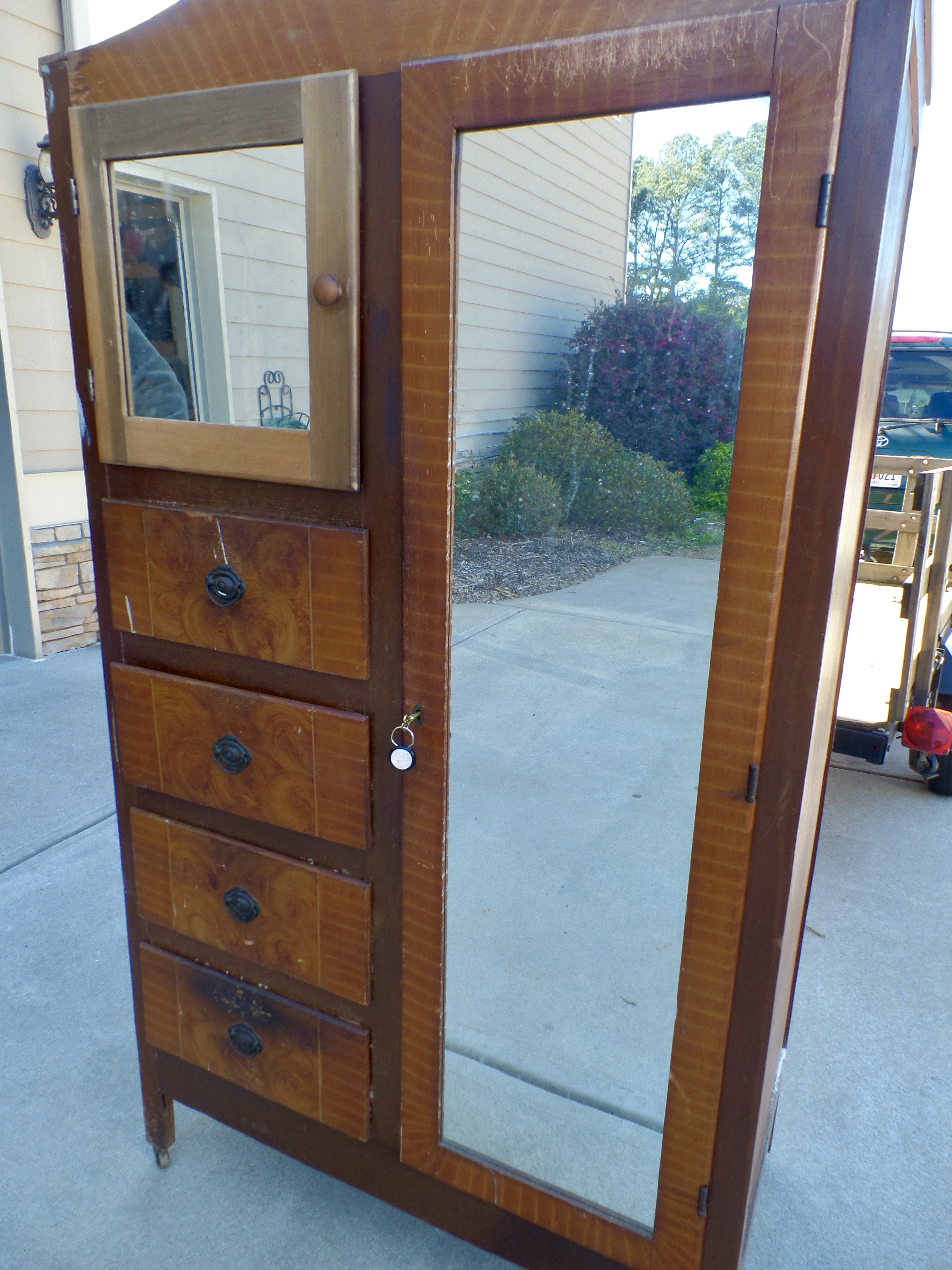 An antique chiffarobe with mirrors sits outside on the driveway of a home.