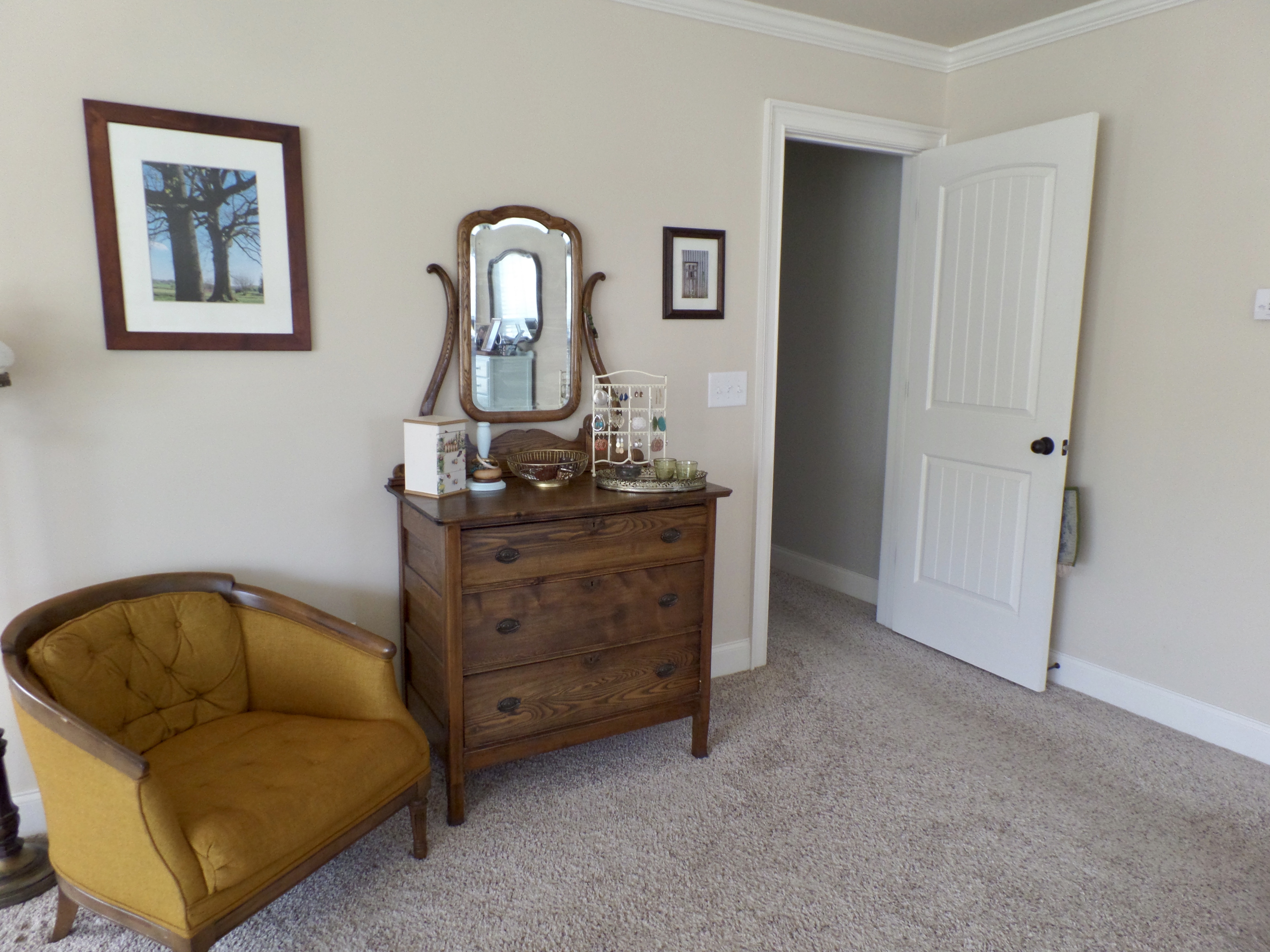 An antique chest of drawers with an attached mirror next to the door of a master bedroom.
