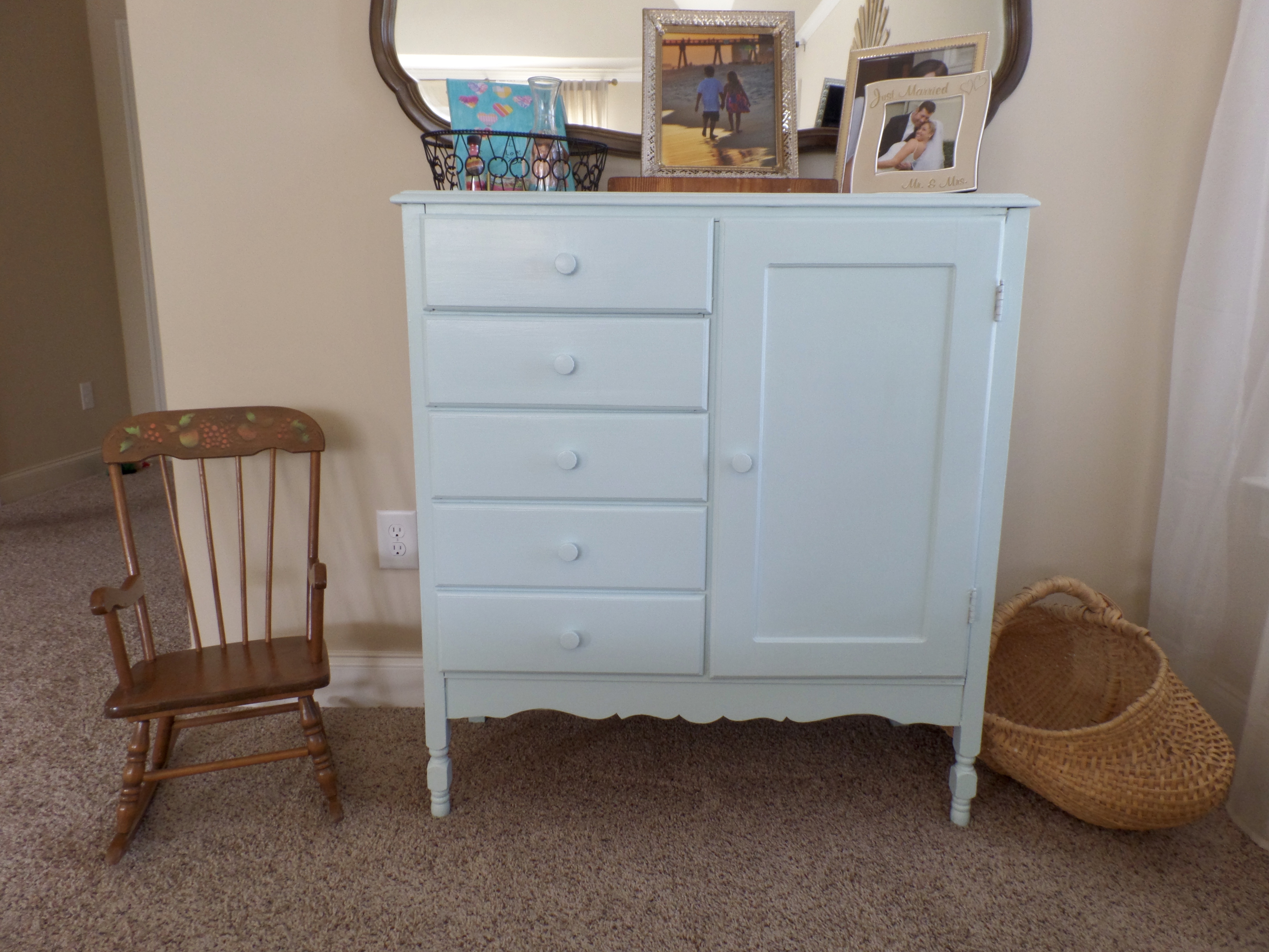A blue antique dresser and mirror in the corner of a master bedroom.