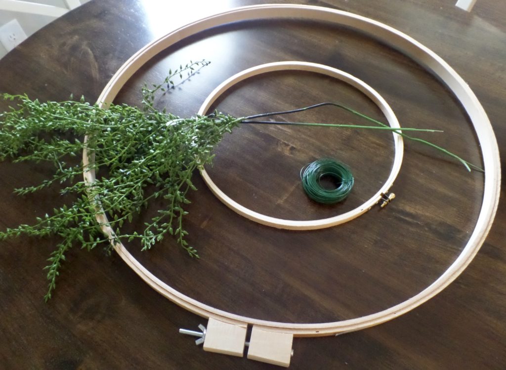 Materials to make a floral hoop wreath, including faux greenery picks, green wire, and two sizes of wooden hoops.