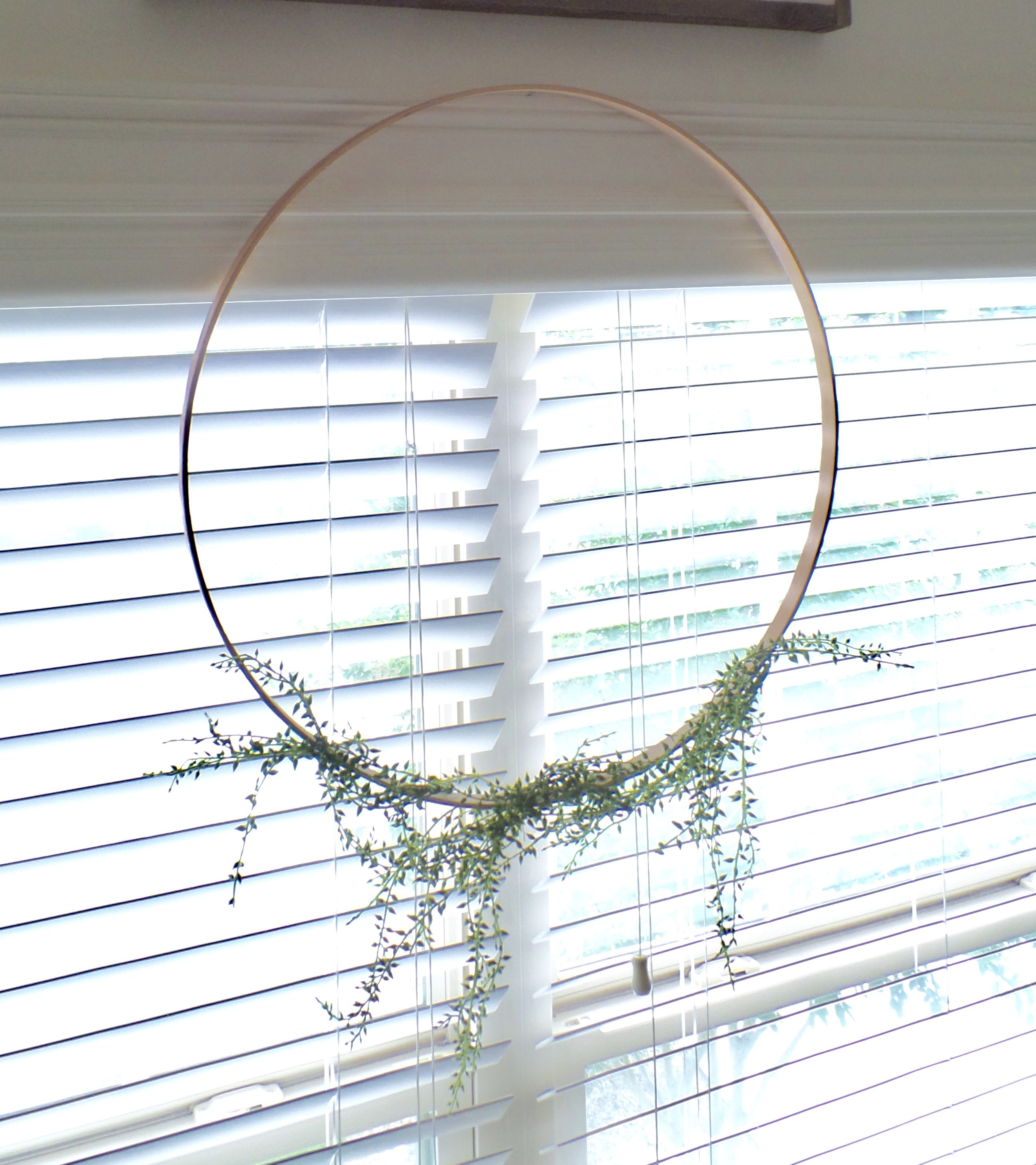 A wooden wreath made from an embroidery hoop with greenery hanging from the bottom.