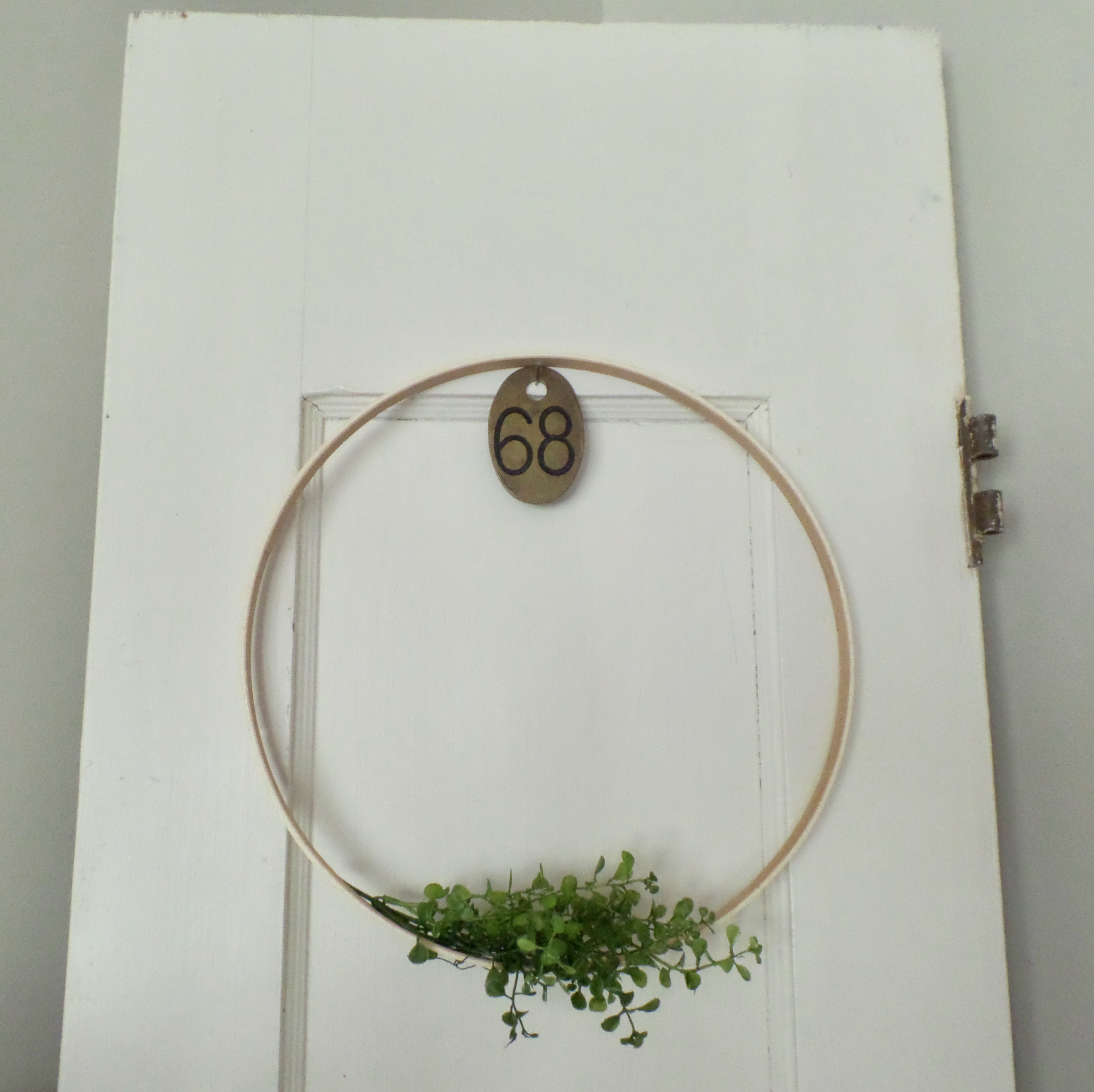 A floral hoop wreath hangs from an unattached white door leaning against a wall.