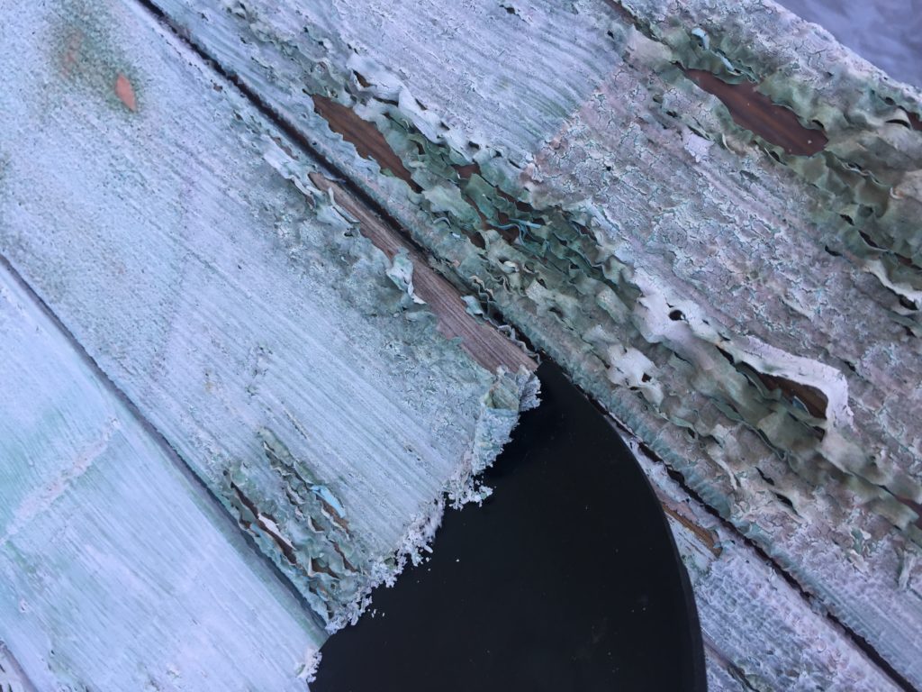 Scraping paint off a wooden planter shelf.