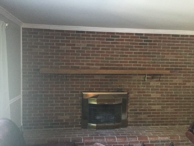 A brick fireplace with brown and red bricks, a wood mantel, and a brass surround.