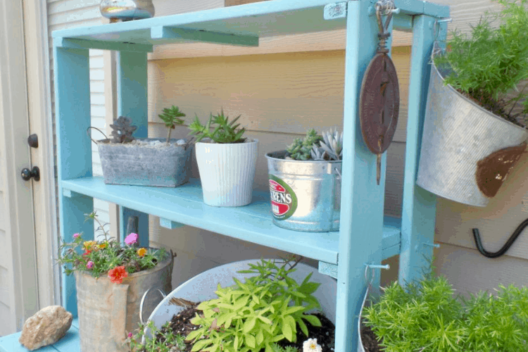 A bright blue plant shelf filled with potted plants on a porch outdoors.