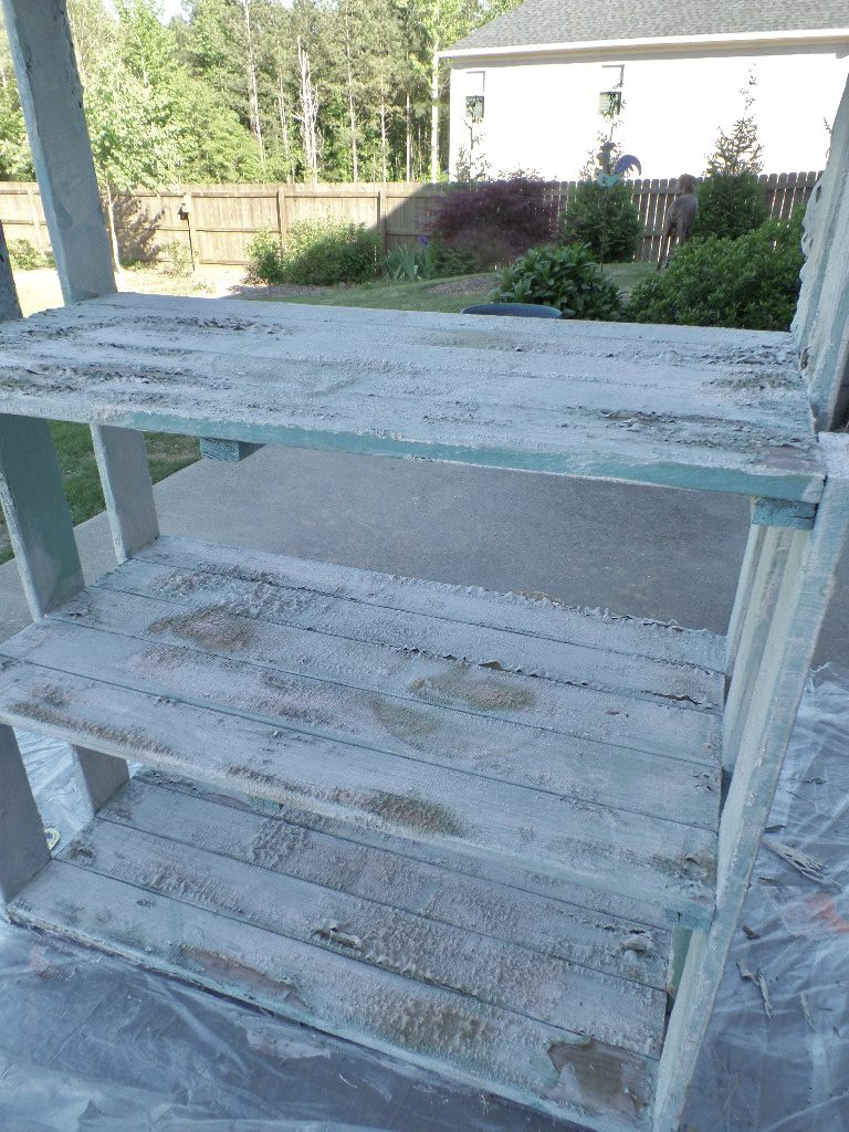 Wood stripper applied to teal paint on a planter shelf.