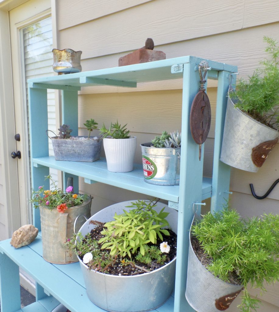 A blue shelf with lots of different potted plants on the side of a house.