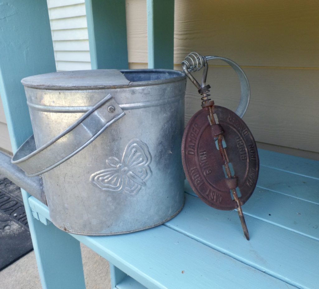 A metal watering can on a blue planter stand.