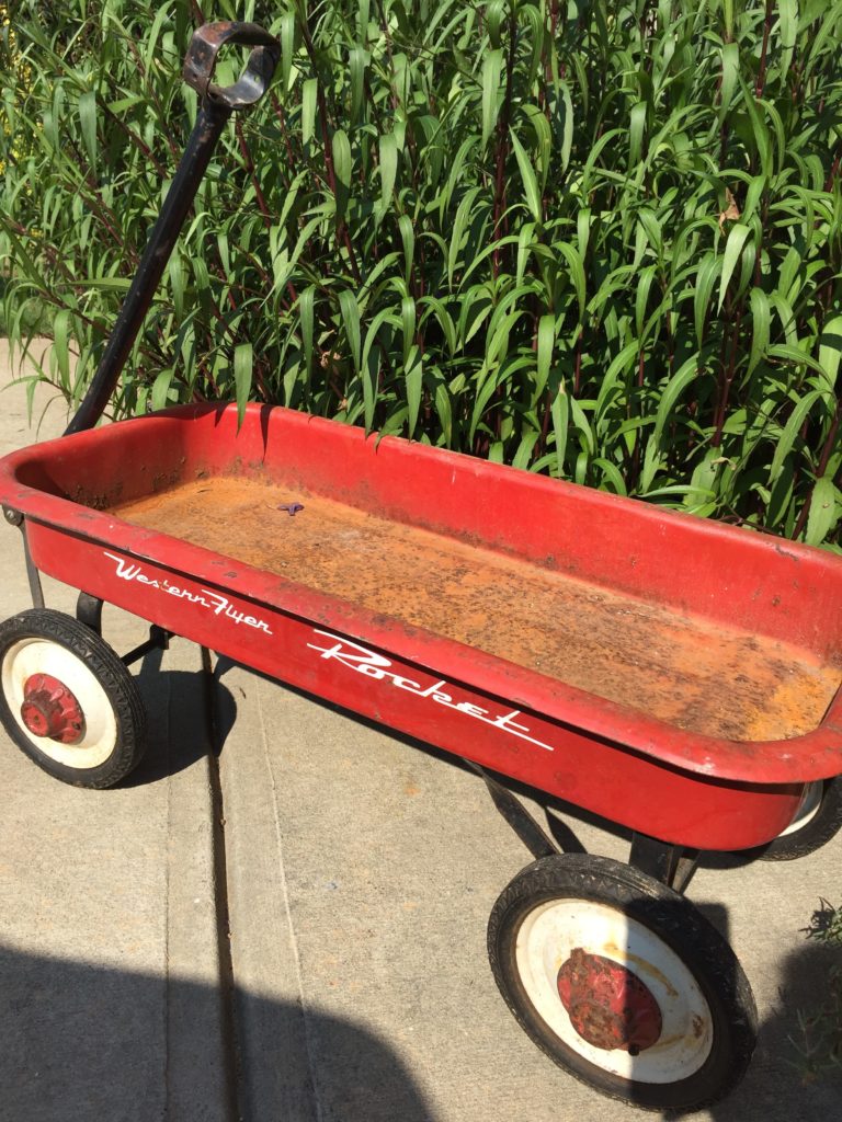 A small rusty red wagon outside on a sidewalk.