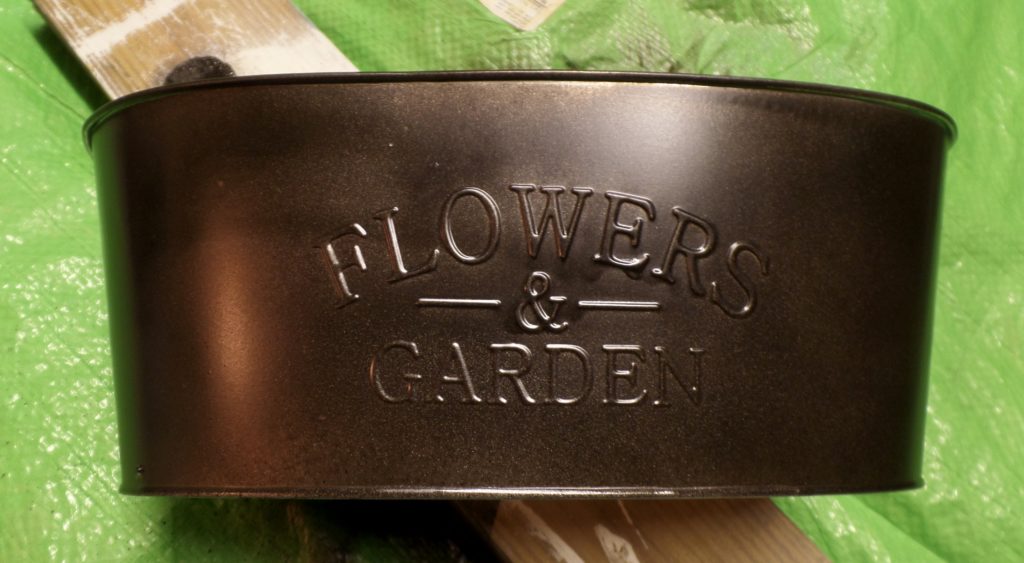 Close-up of a metal tub with the words \"Flowers & Garden\" inscribed on the front.