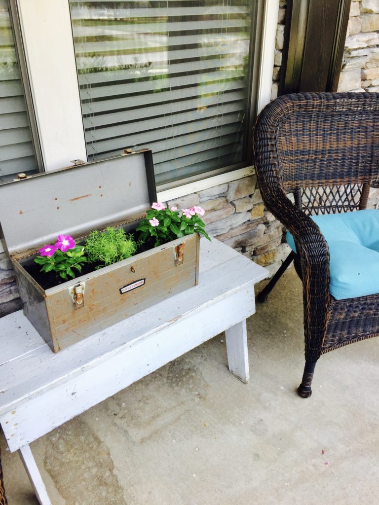 A craftsman toolbox planter with pink and purple flowers on a front porch.