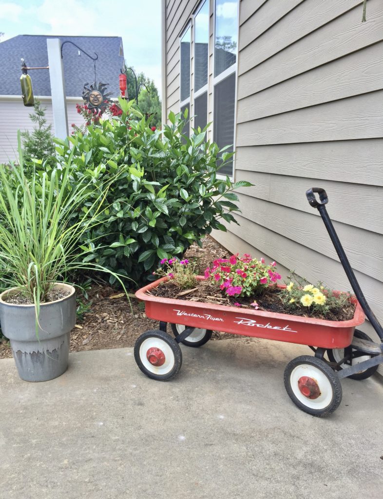 A red wagon with dirt and flowers growing inside.