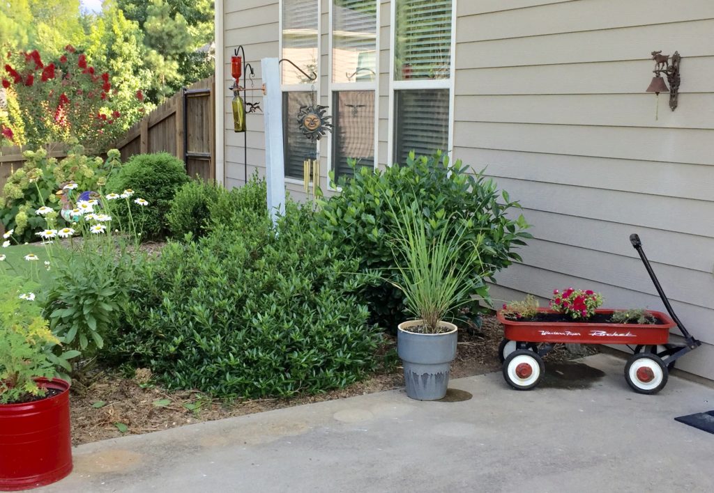 A red wagon planter with flowers on the side of a house.