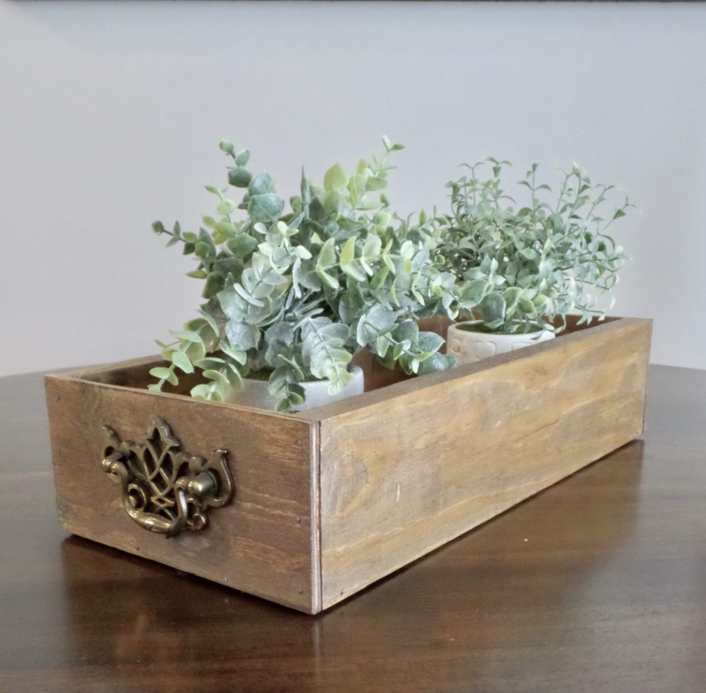 Wooden farmhouse crate with two faux plants in white pots.