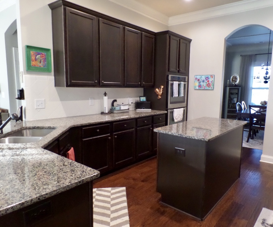 A kitchen with dark brown cabinets and tan granite countertops.