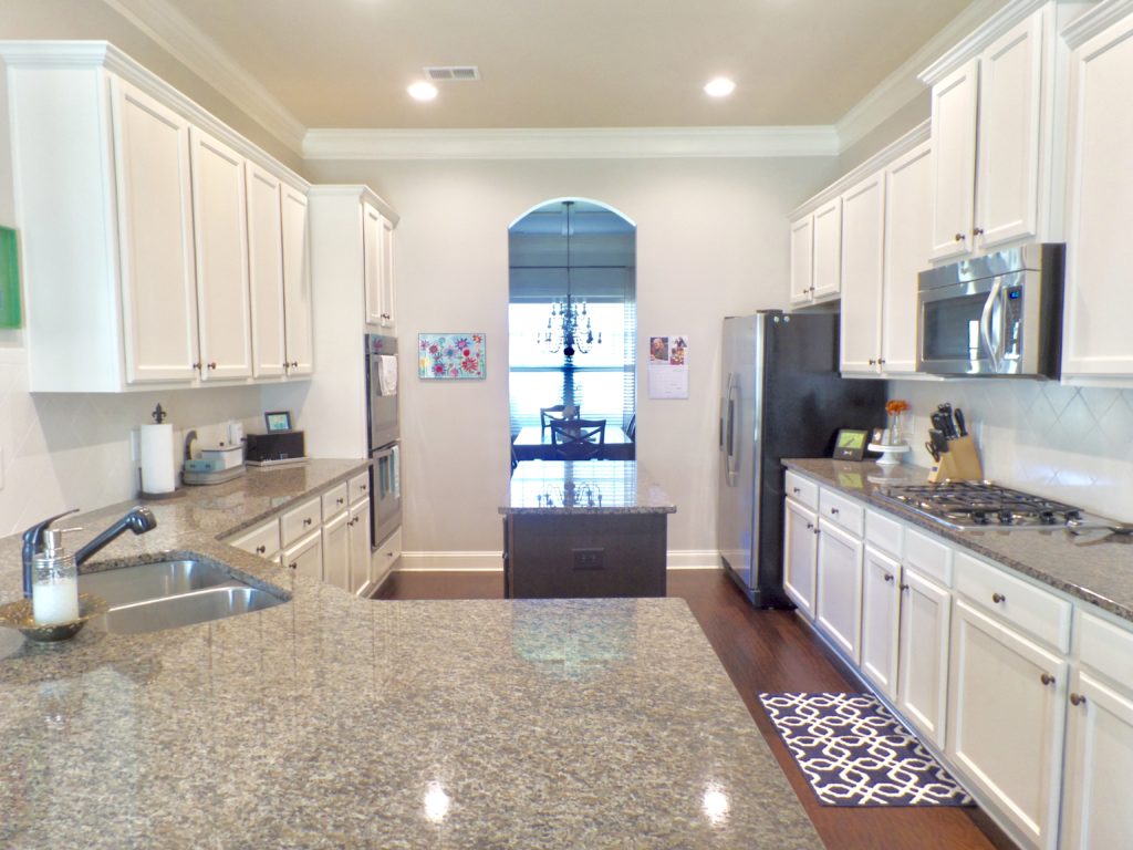 A kitchen with white cabinets and tan granite countertops.