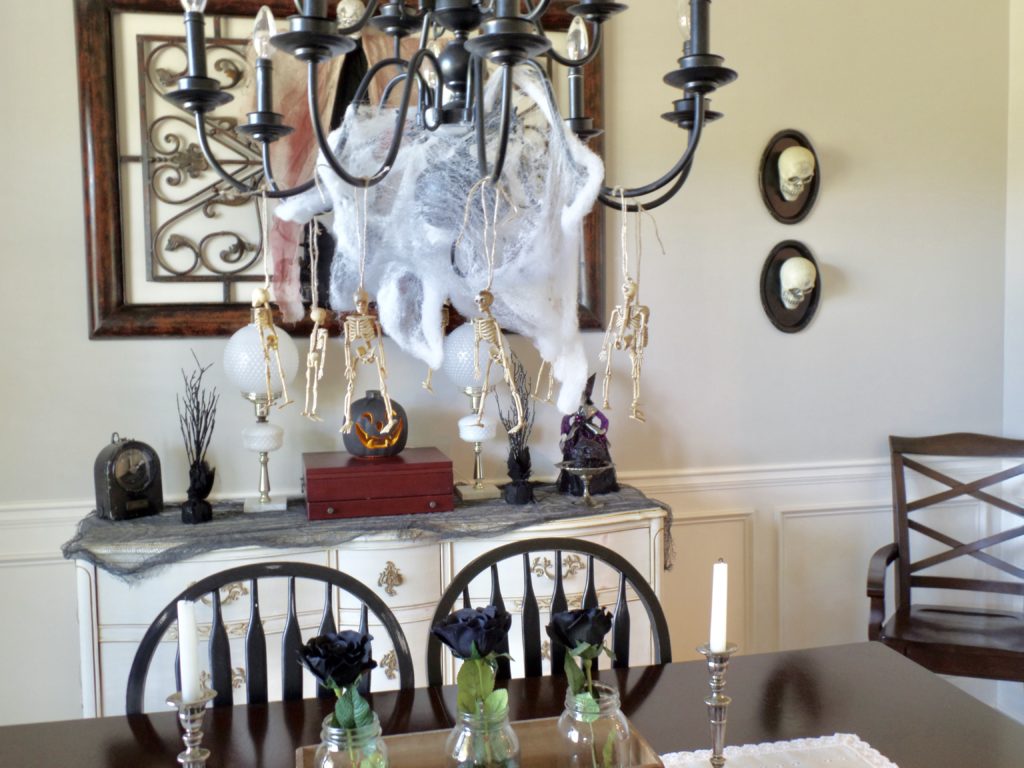 Halloween decor in a dining room including skulls on a wall and cobwebs in a chandelier. 