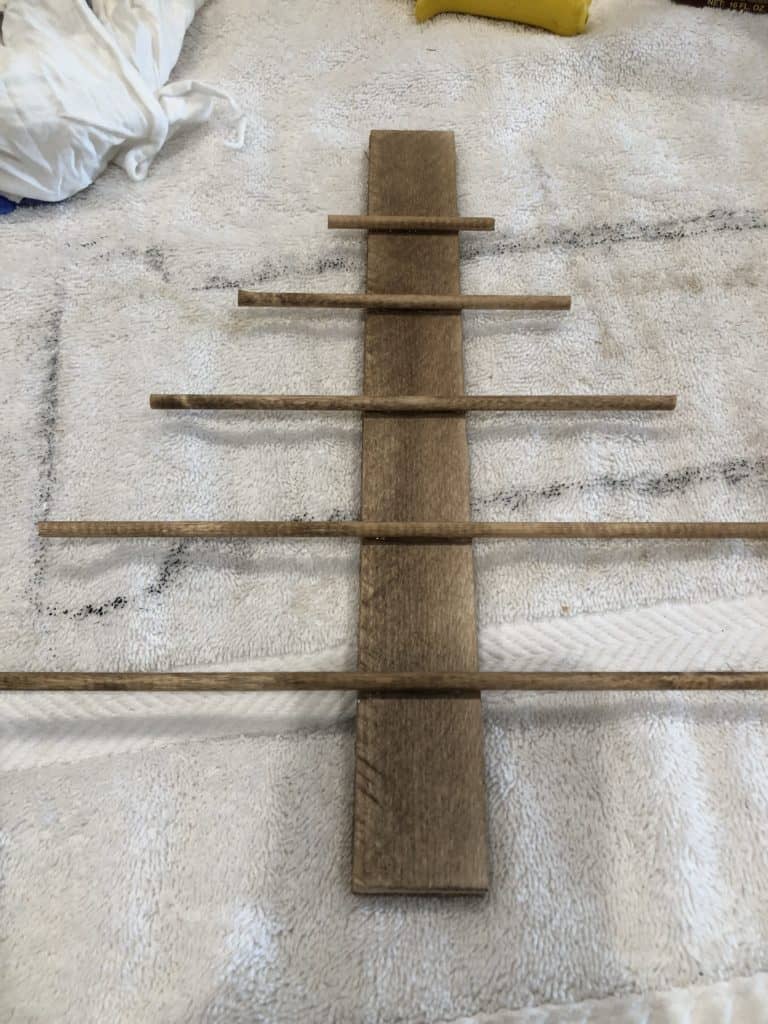 A strip of wood and dowel rods in the shape of a Christmas tree.