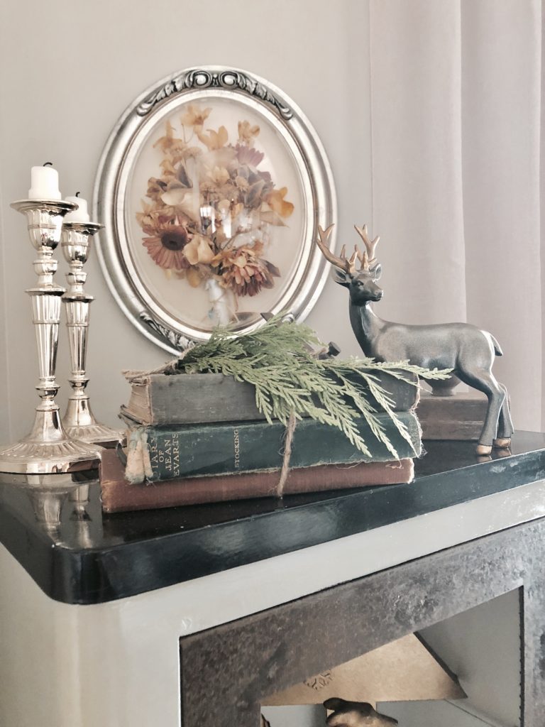 A reindeer statue, antique books, and gold candlesticks on top of an antique medicine cabinet.