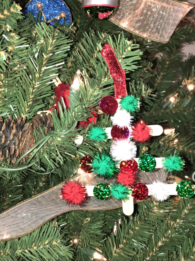 A green and red homemade Christmas tree ornament hanging from a Christmas tree.