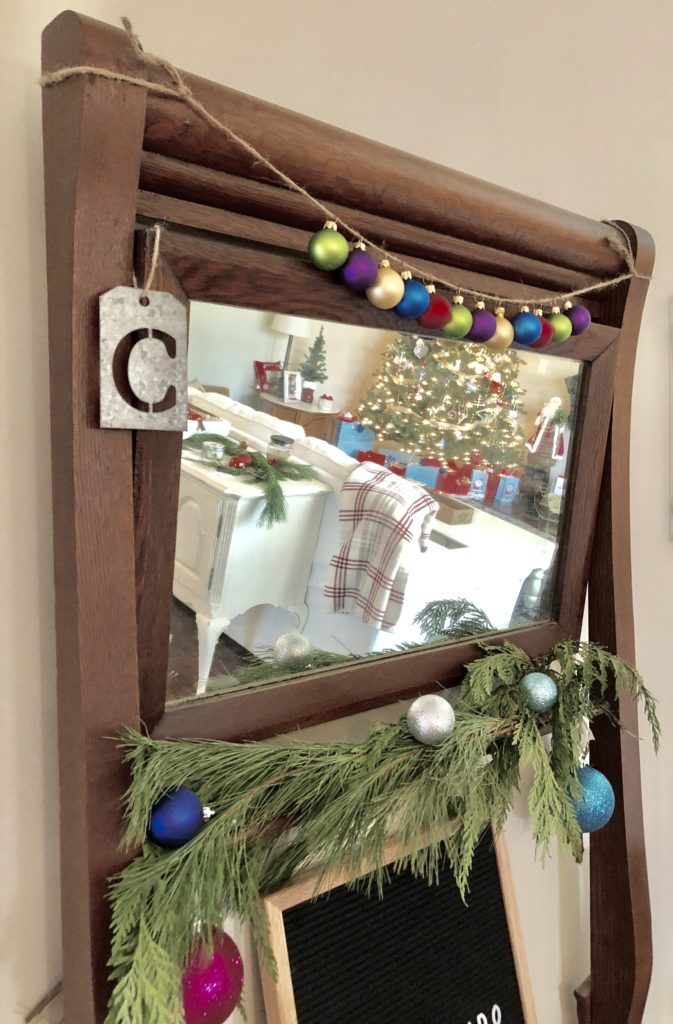 A mirror decorated with a Christmas ornament garland and fir tree branches.