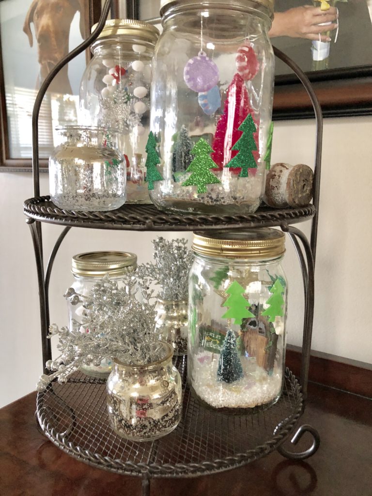 DIY snow globes on a display stand on top of an entryway table.