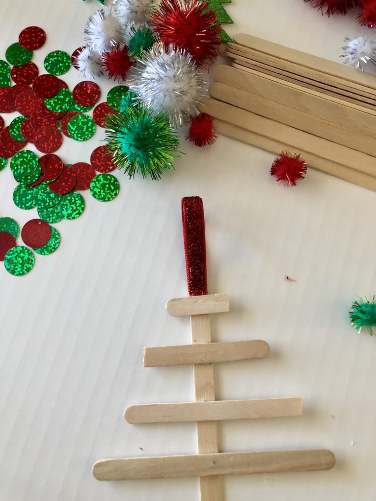 A Christmas tree made out of popsicle sticks with green and red craft supplies as decorations.