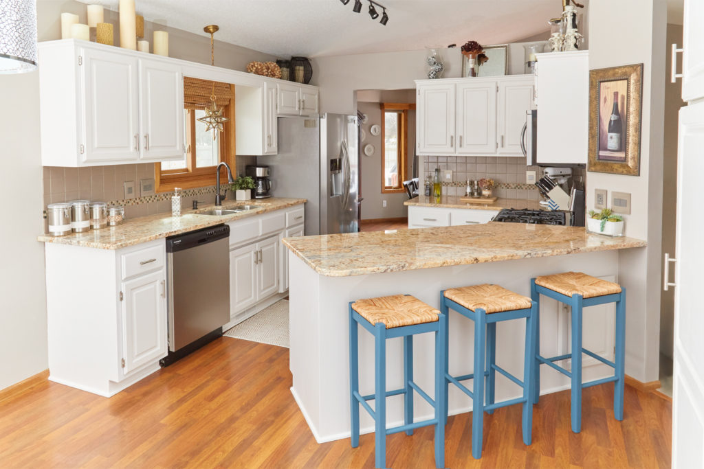 A white kitchen with an angled peninsula, tan countertops, and blue barstools