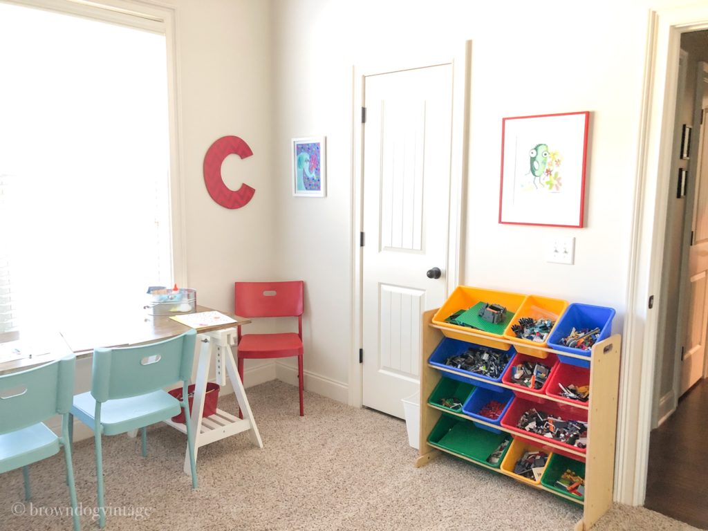 A tidy playroom with a primary colored storage system a desk with a blue chair and wall art.