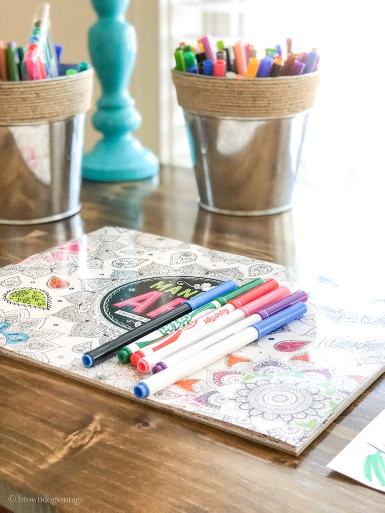 An adult coloring book and markers on a wooden desk.