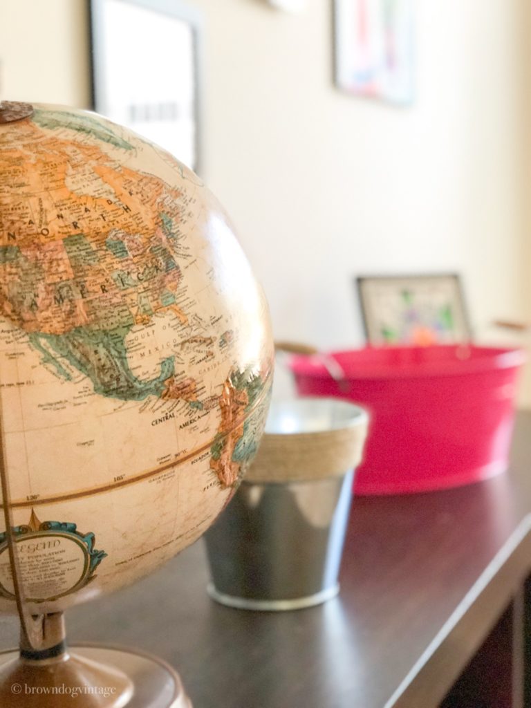 Close-up of an old globe on a shelf with a pink storage bin.