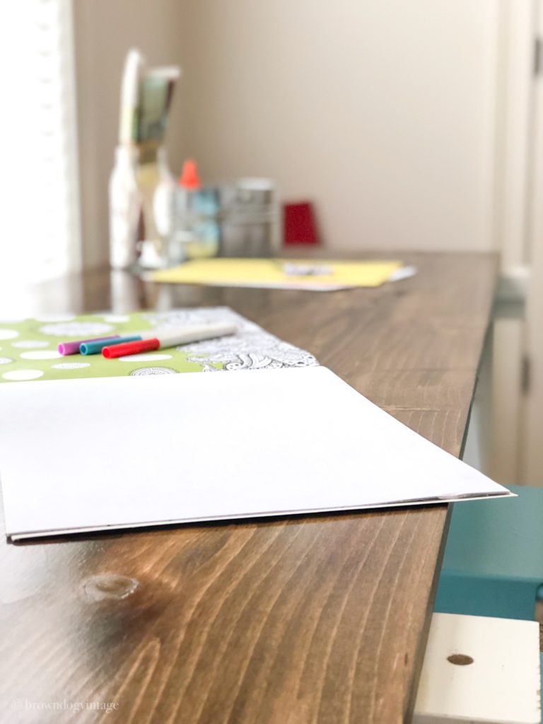 Close-up of a wooden desk top with coloring books and art supplies on top.