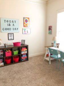 A playroom with open storage shelves and a desk under a large window.