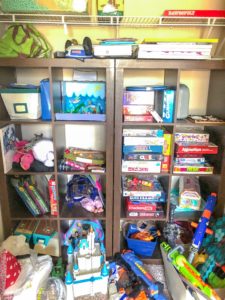 Cluttered playroom shelves with games, books, and toys.