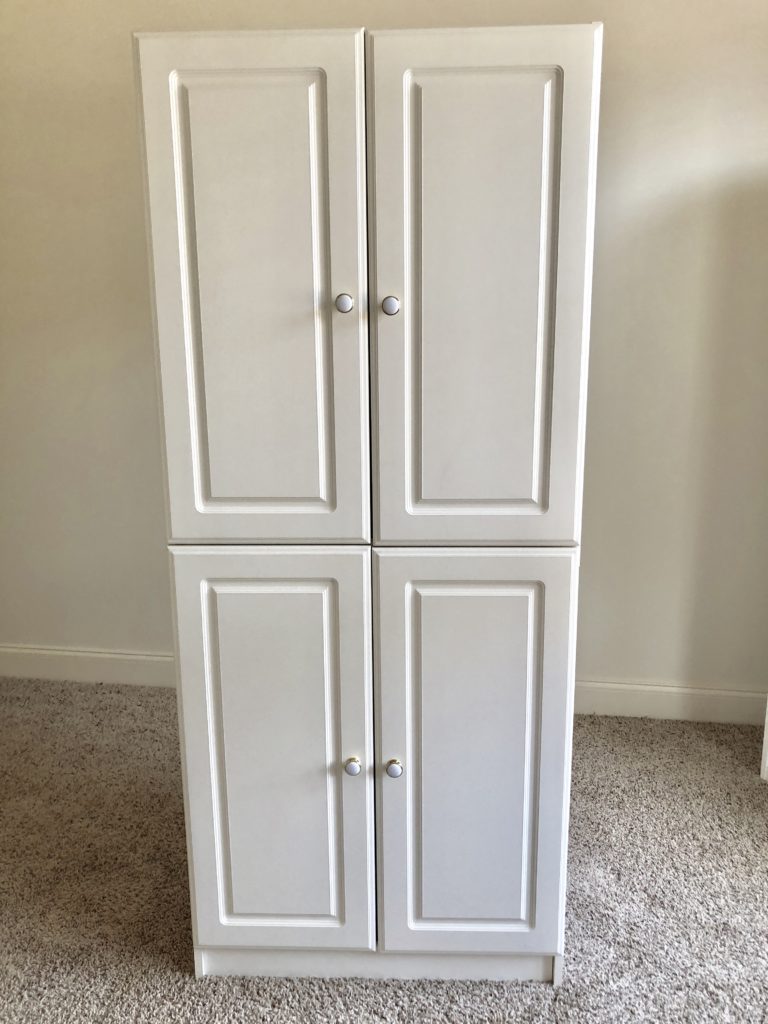 A tall white storage cabinet in a room with tan carpet and cream-colored walls.