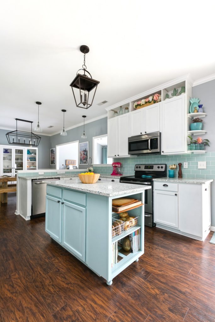 A kitchen with a teal backsplash and island and white cabinets.