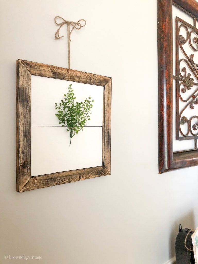 greenery on a white background with a rustic wooden frame hanging on a wall in a dining room.