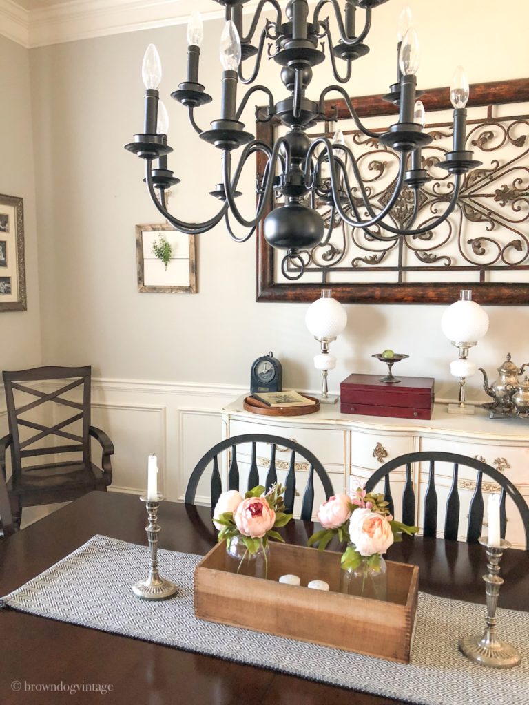 A dining room table with pink faux flowers, candles, and a table runner