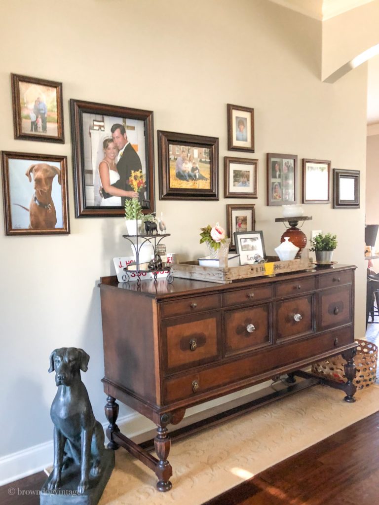 An antique wooden side table in an entryway with flowers and greenery on top.