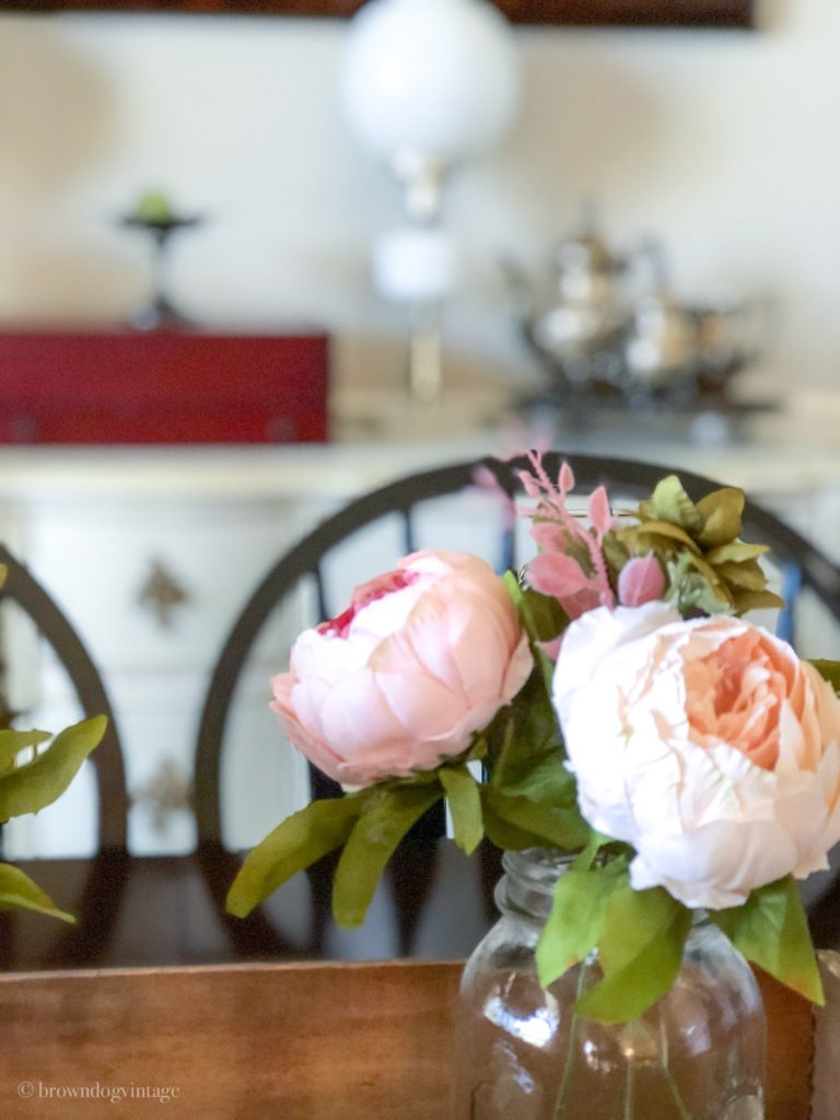 Close up of faux pink flowers in a glass vase inside a rustic wooden box on a dining room table.